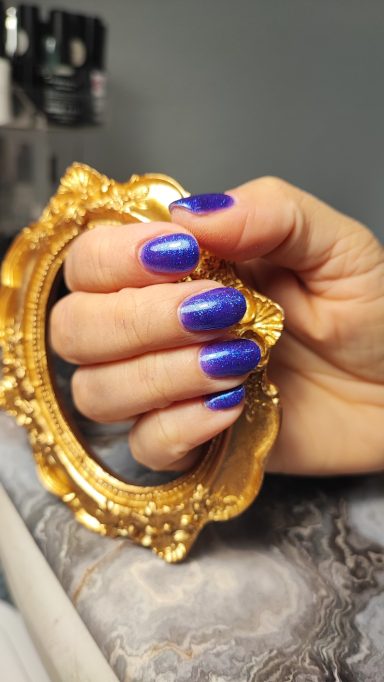 Eine Hand mit blauen Nägeln hält einen goldenen Rahmen.